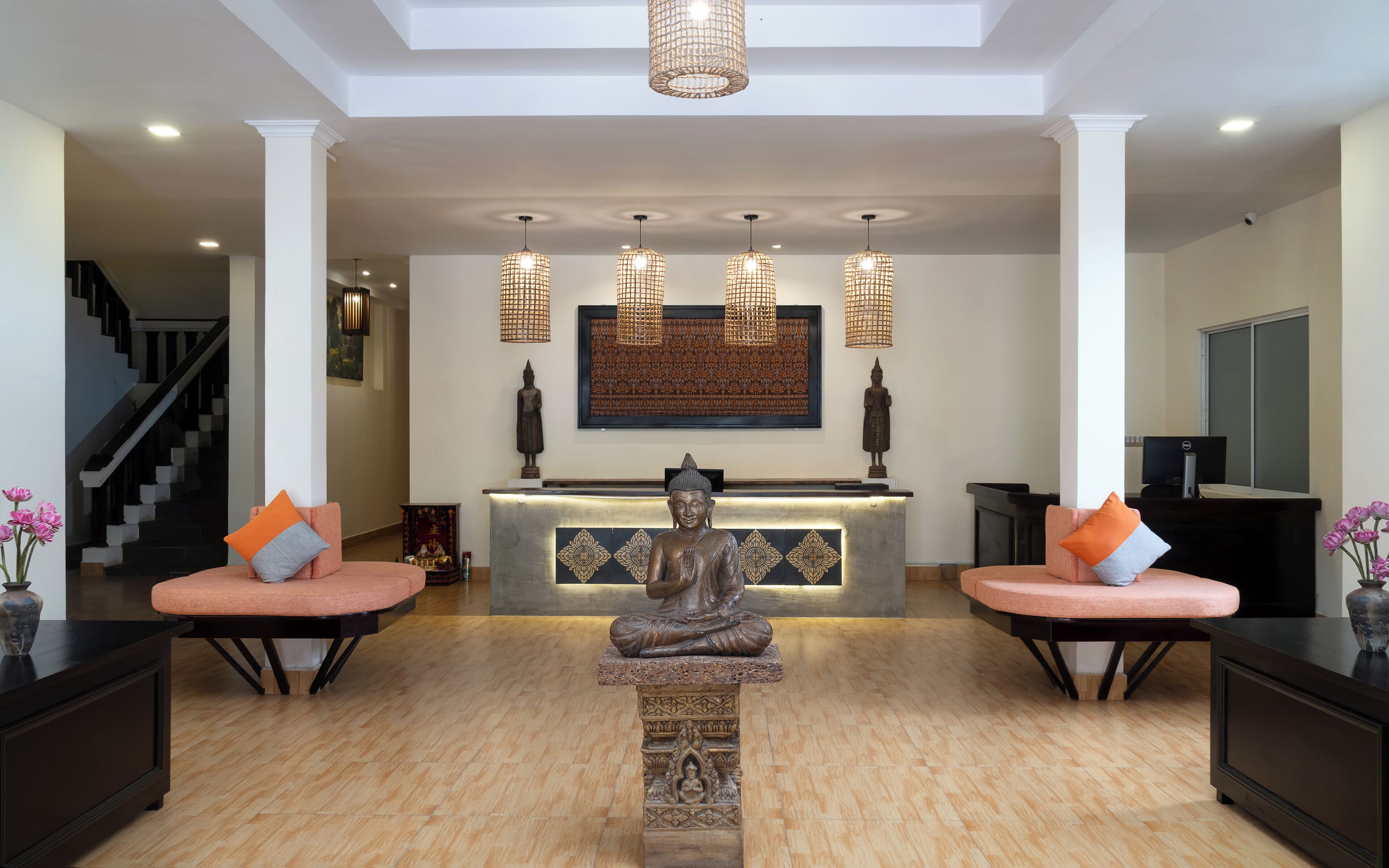 Un área de recepción con una estatua de Buda, dos sofás con cojines naranjas, una escalera y una gran obra de arte enmarcada en la pared.
