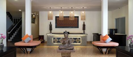 Un área de recepción con una estatua de Buda, dos sofás con cojines naranjas, una escalera y una gran obra de arte enmarcada en la pared.