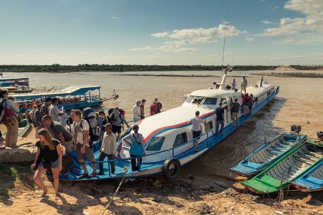 A boat with passengers boarding, surrounded by calm water and a clear sky.