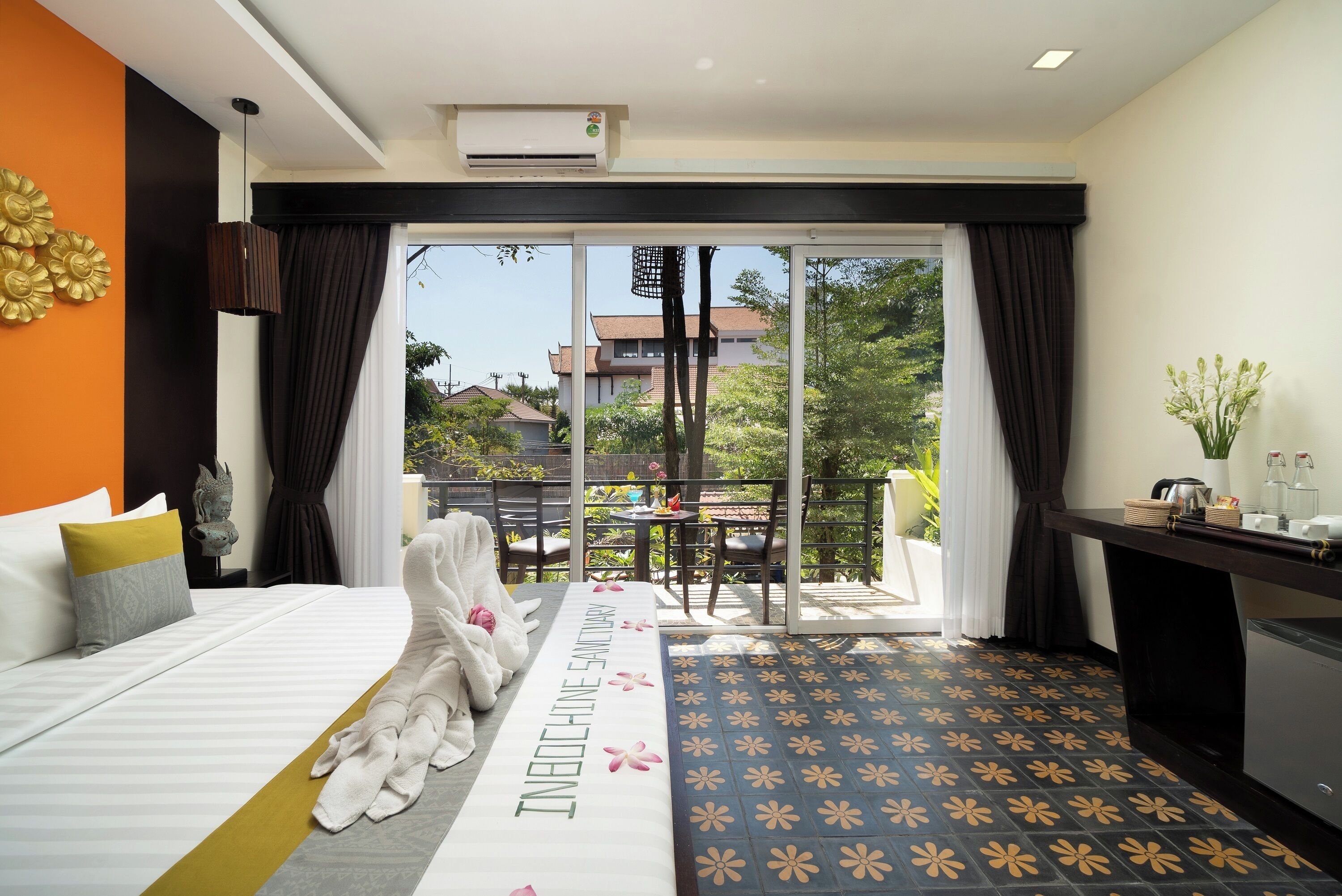 A hotel room with a bed, a table with a vase, and a view of the outside.
