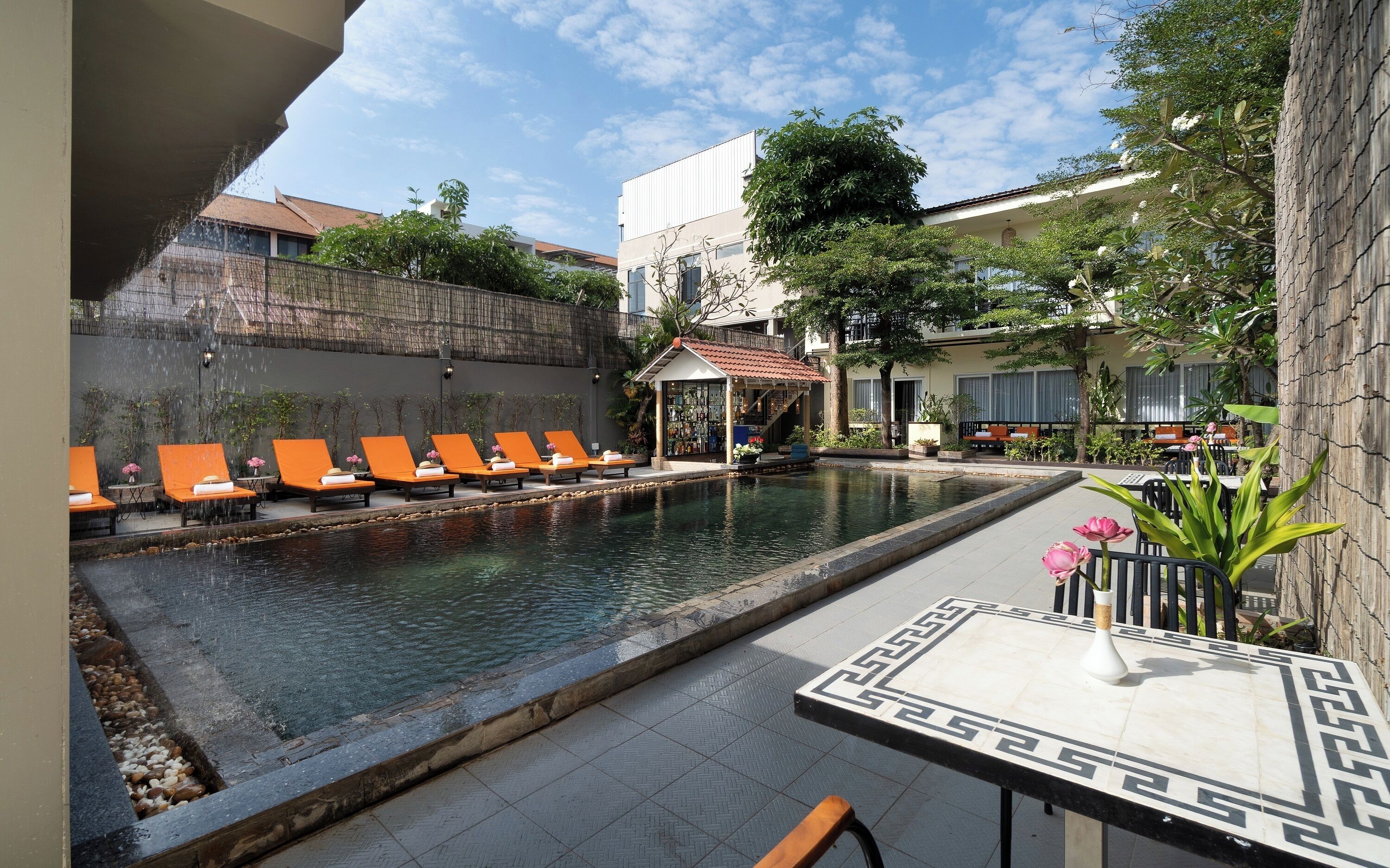 A pool area with lounge chairs, a bar, and a small pavilion.