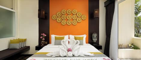 Quarto de hotel com cama, almofadas, um vaso com flores, um objeto decorativo na parede e uma janela com cortinas.