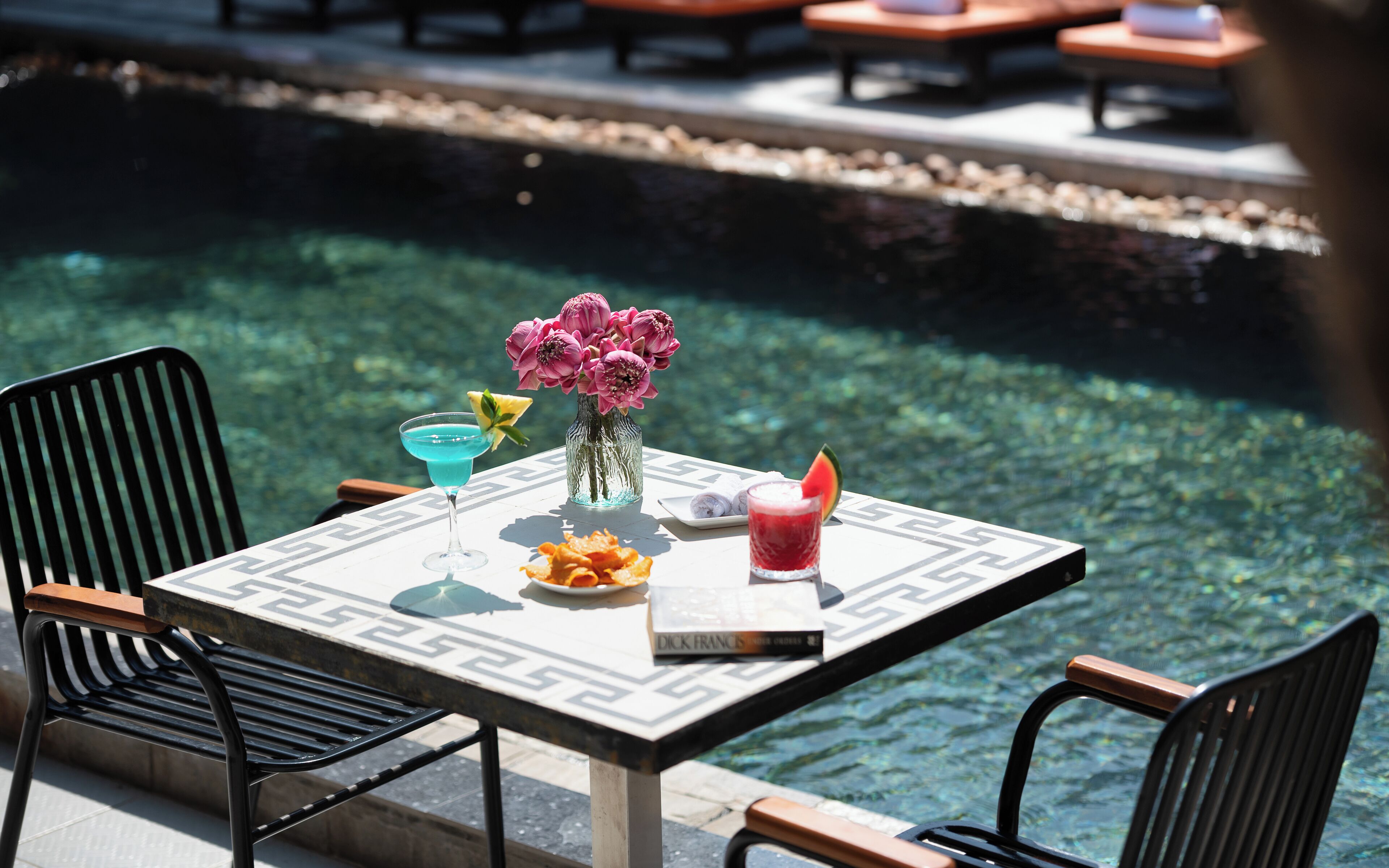 A table with a drink, flowers, and a book by Dick Francis.