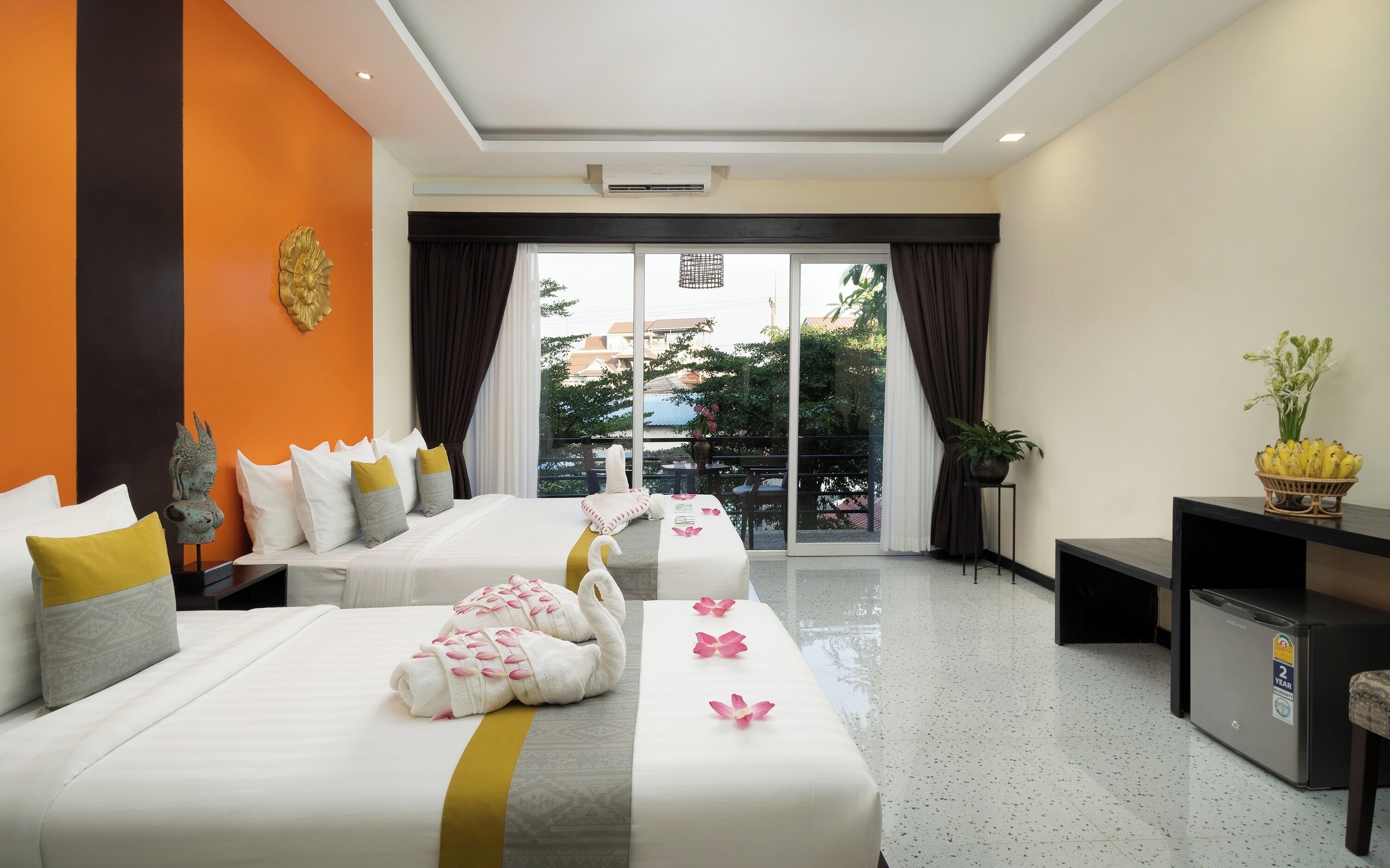 A hotel room with two beds, a small table, a TV, and a balcony with a view.