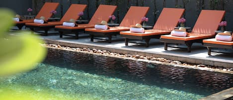 Zona de piscina con sillones de descanso y una piscina cristalina.