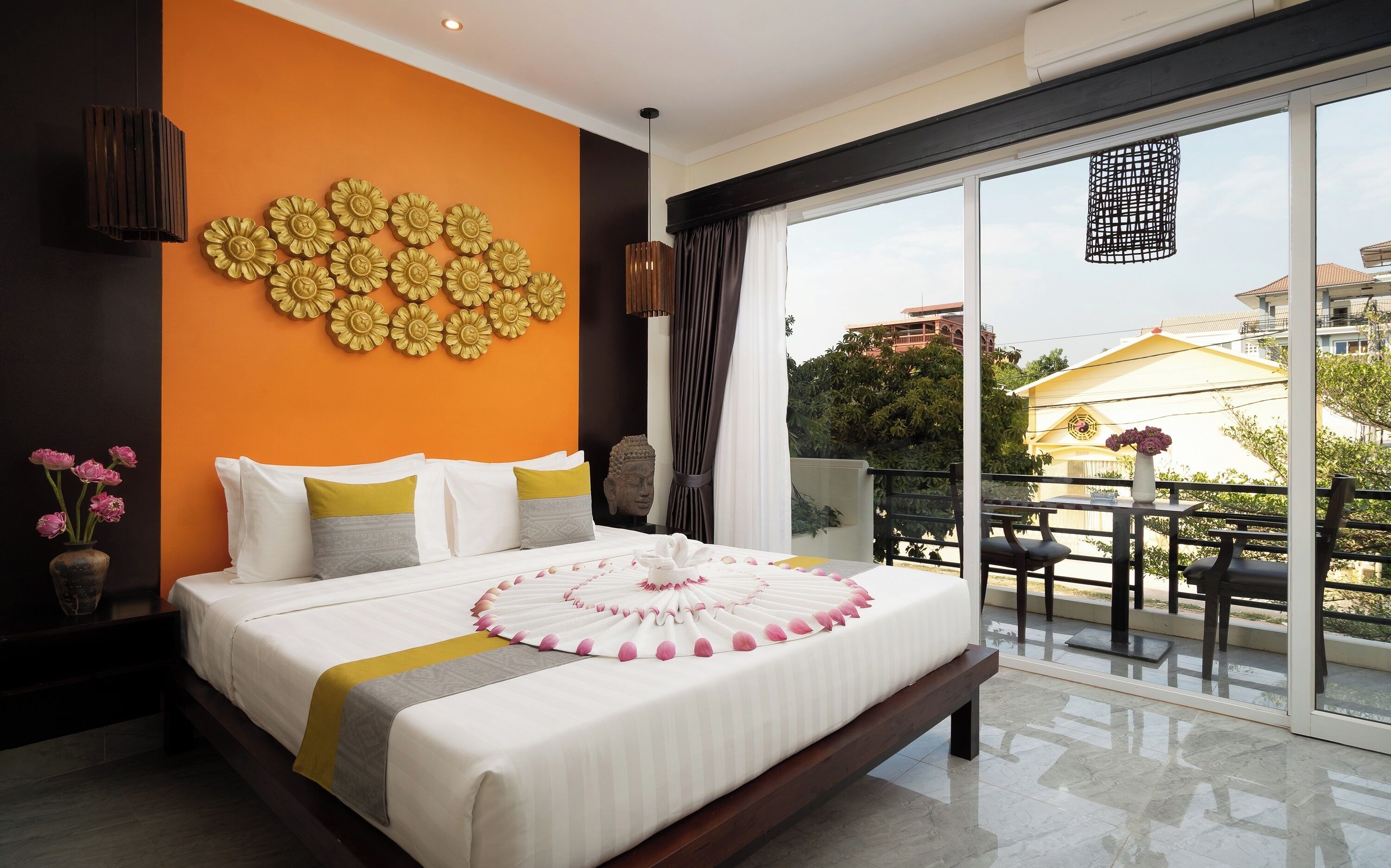 A modern hotel room with a large bed, a decorative wall, and a balcony with outdoor seating.