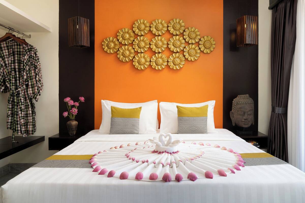 Une chambre d’hôtel avec un lit, un mur décoré de motifs floraux, une statue de Bouddha et une fenêtre avec des rideaux.