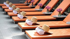 A row of sun loungers with towels and hats, each with a small vase of flowers.