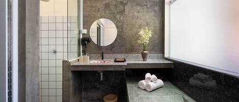 Un baño con ducha, lavamanos con espejo, un jarrón con flores y toallas en el suelo.