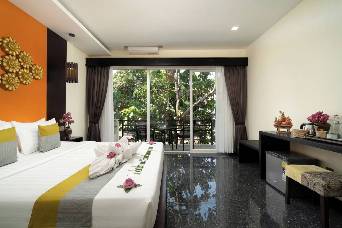 Une chambre d’hôtel comprenant un lit, un bureau, une chaise, une petite table et un balcon avec vue sur les arbres.