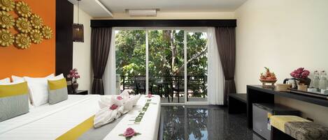 Une chambre d’hôtel comprenant un lit, un bureau, une chaise, une petite table et un balcon avec vue sur les arbres.