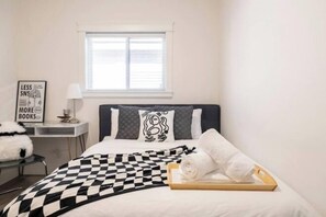 A bedroom with a checkered bedspread, a bedside table with a lamp, a framed quote on the wall, and a window above the bed. - Sweet Home-Separate Entry-Near YVR Airport & Skytrain & Costco (Greater Vancouver)
