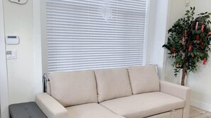 A beige sectional sofa in a room with a window, a small bench, and a decorative plant. - Sweet Home-Separate Entry-Near YVR Airport & Skytrain & Costco (Greater Vancouver)