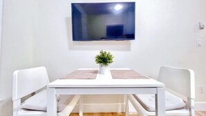 A dining area with a white table, two white chairs, a potted plant, and a flat-screen TV mounted on the wall. - Sweet Home-Separate Entry-Near YVR Airport & Skytrain & Costco (Greater Vancouver)