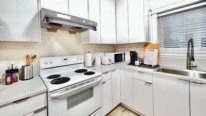 A modern kitchen with white cabinets, a stove, a microwave, and a sink. - Sweet Home-Separate Entry-Near YVR Airport & Skytrain & Costco (Greater Vancouver)