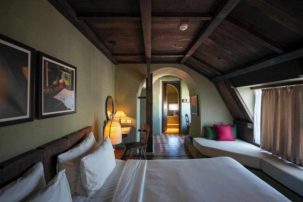 Une chambre d’hôtel avec un grand lit, un bureau avec une lampe, une chaise et une vue sur un couloir.