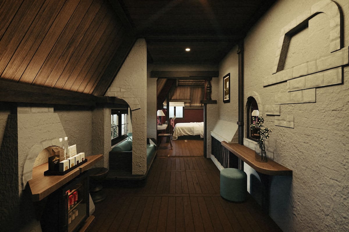 Un couloir étroit, doté d’un plancher en bois, avec un plafond haut et des murs en pierre. On aperçoit un lit au loin, et des bancs sont disposés le long du couloir.