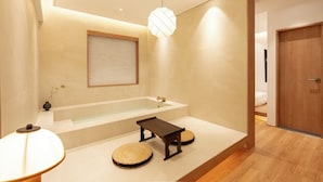 A modern bathroom with a freestanding bathtub, a wooden bench, and a round woven stool. - Haeundae Toyu Ryokan (Busan)