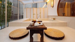 A modern interior with a wooden table, two woven poufs, a white teapot, and a small bowl on a platform. - Haeundae Toyu Ryokan (Busan)