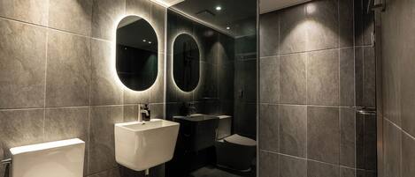 Une salle de bain moderne comprenant des toilettes, un lavabo et un espace douche, avec des carreaux foncés et une cloison en verre.