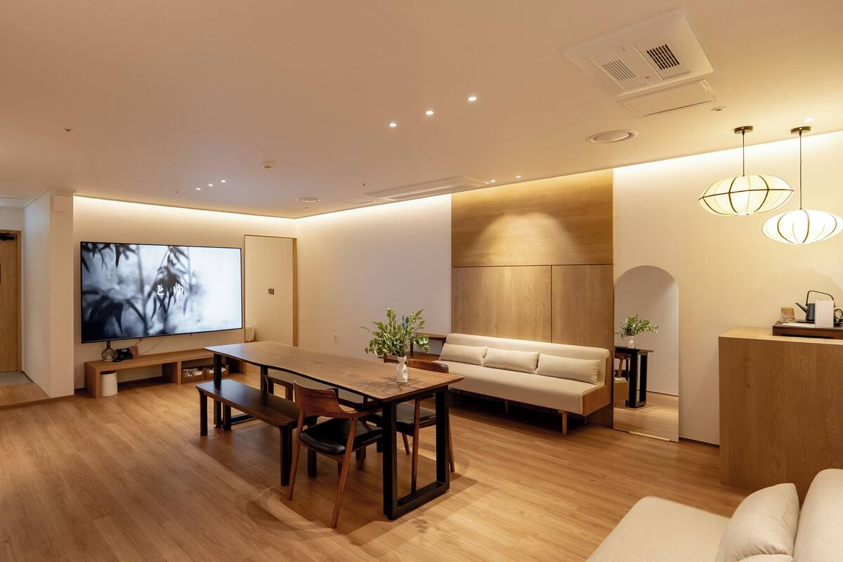 A modern living room with a wooden dining table, sofa, and TV.