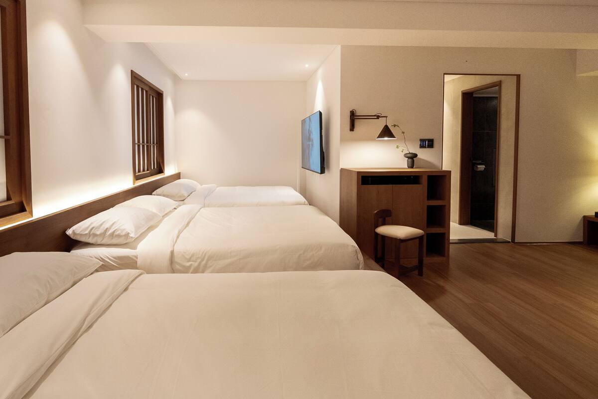 A hotel room with two beds, a desk, a chair, and a door.