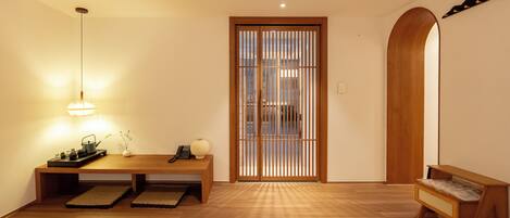 Un interior japonés tradicional con suelo de madera, un acceso con estera de tatami, una mesa baja con tetera y juego de té, y un fusuma con listones verticales.