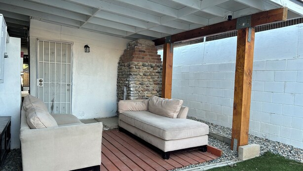 En overdækket terrasse med en beige sofa og lænestol, en stenvæg og en træpergola.