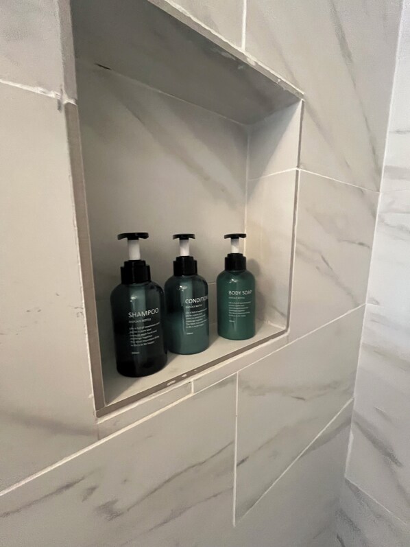Une salle de bain avec un mur en marbre et une étagère contenant trois flacons de produits de soins pour le corps.