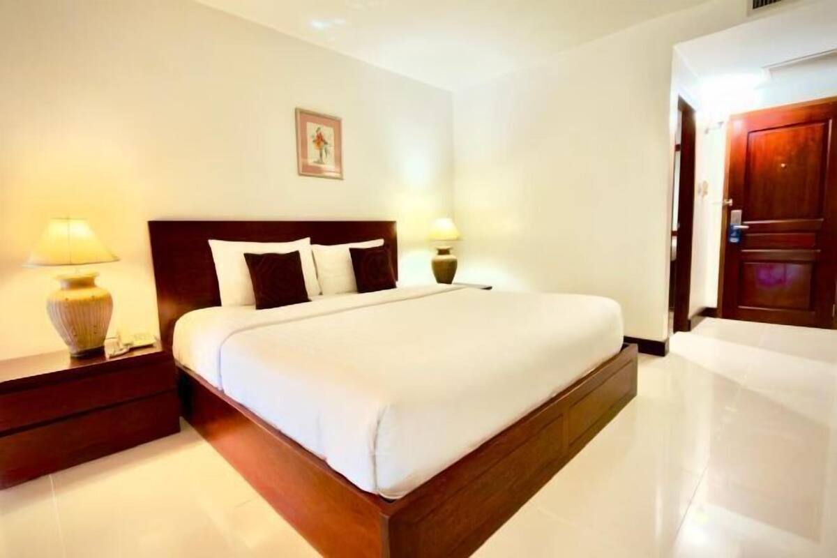 A hotel room with a large bed, bedside tables with lamps, a wooden headboard, and a door with a handle.