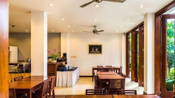 A dining area with wooden tables and chairs, a ceiling fan, and a view of greenery outside. - Sabaidee@Lao Hotel Vientiane (Vientiane)