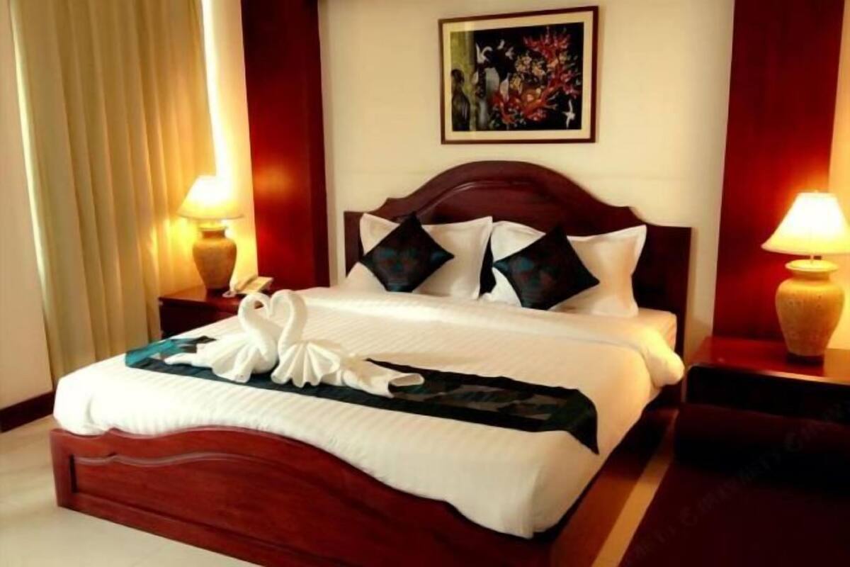 A neatly made bed with a white comforter and decorative pillows, a wooden headboard, and two bedside lamps.