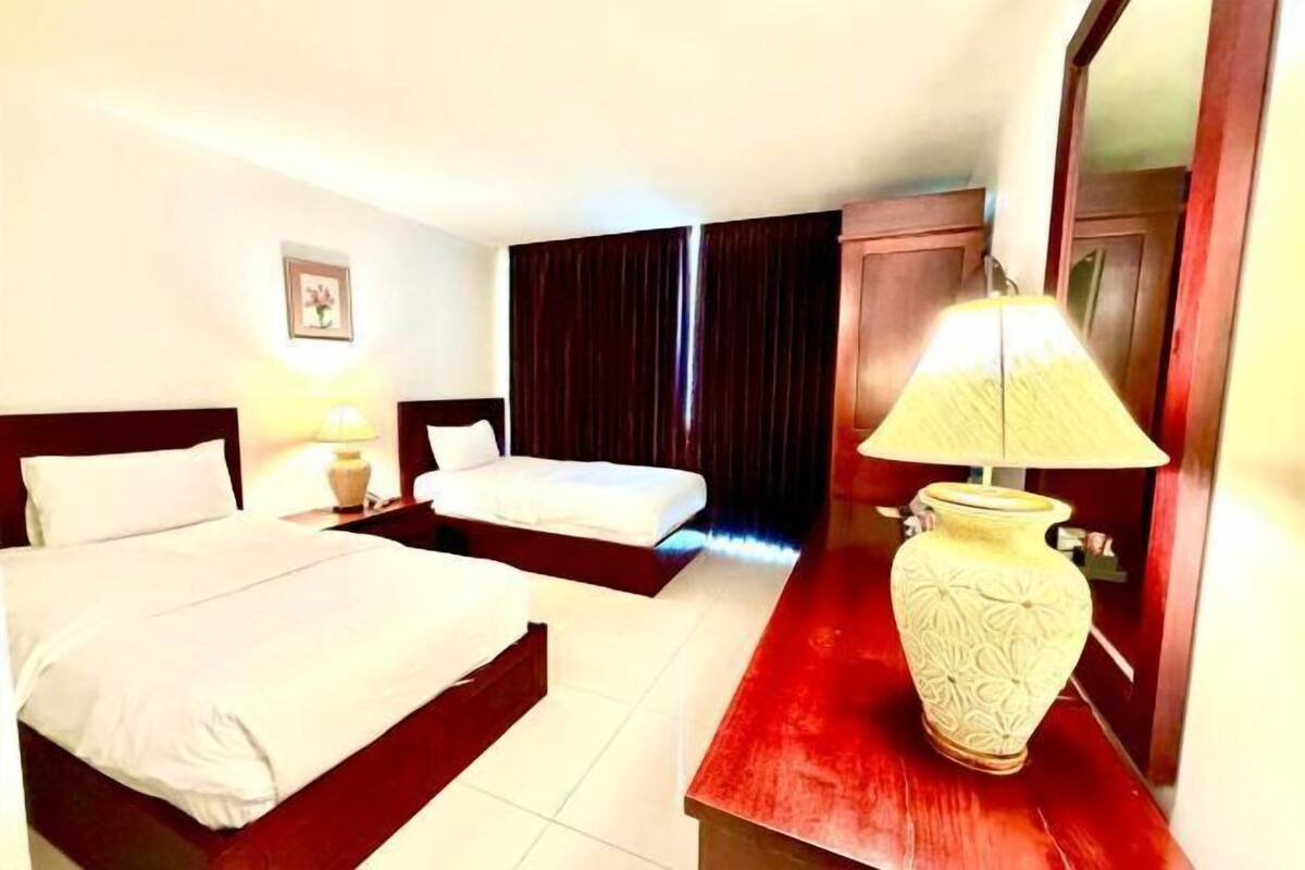 A hotel room with two beds, a nightstand with a lamp, a large vase, and a mirror.