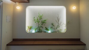 A wall-mounted window with a view of indoor plants and a wooden bench below. - Harujae Myeongdong (Seoul)