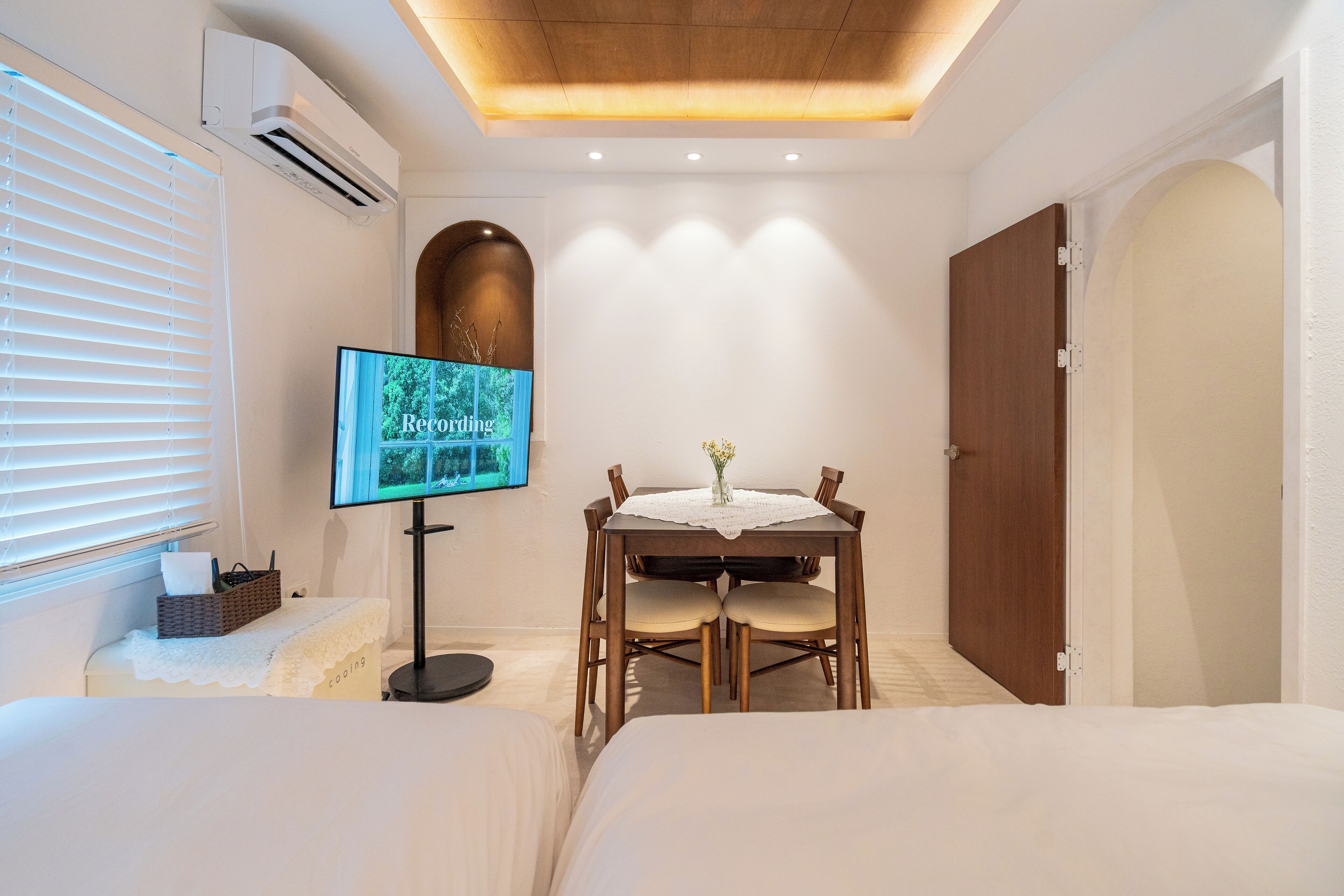 A hotel room with a bed, a TV on a stand, a dining table with chairs, and a wooden door.
