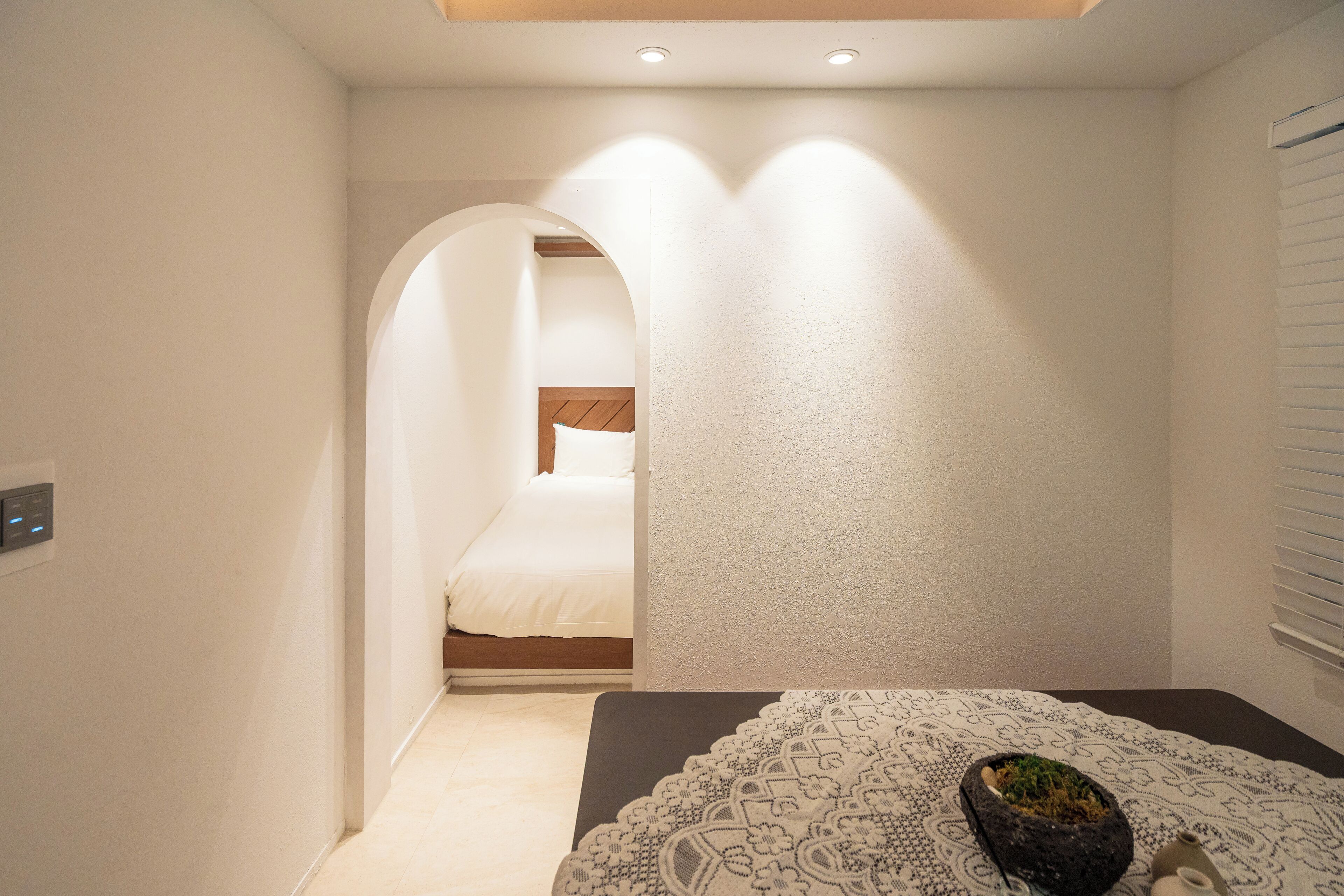 A bedroom with a bed, a bedside table with a decorative item, and a window with blinds.