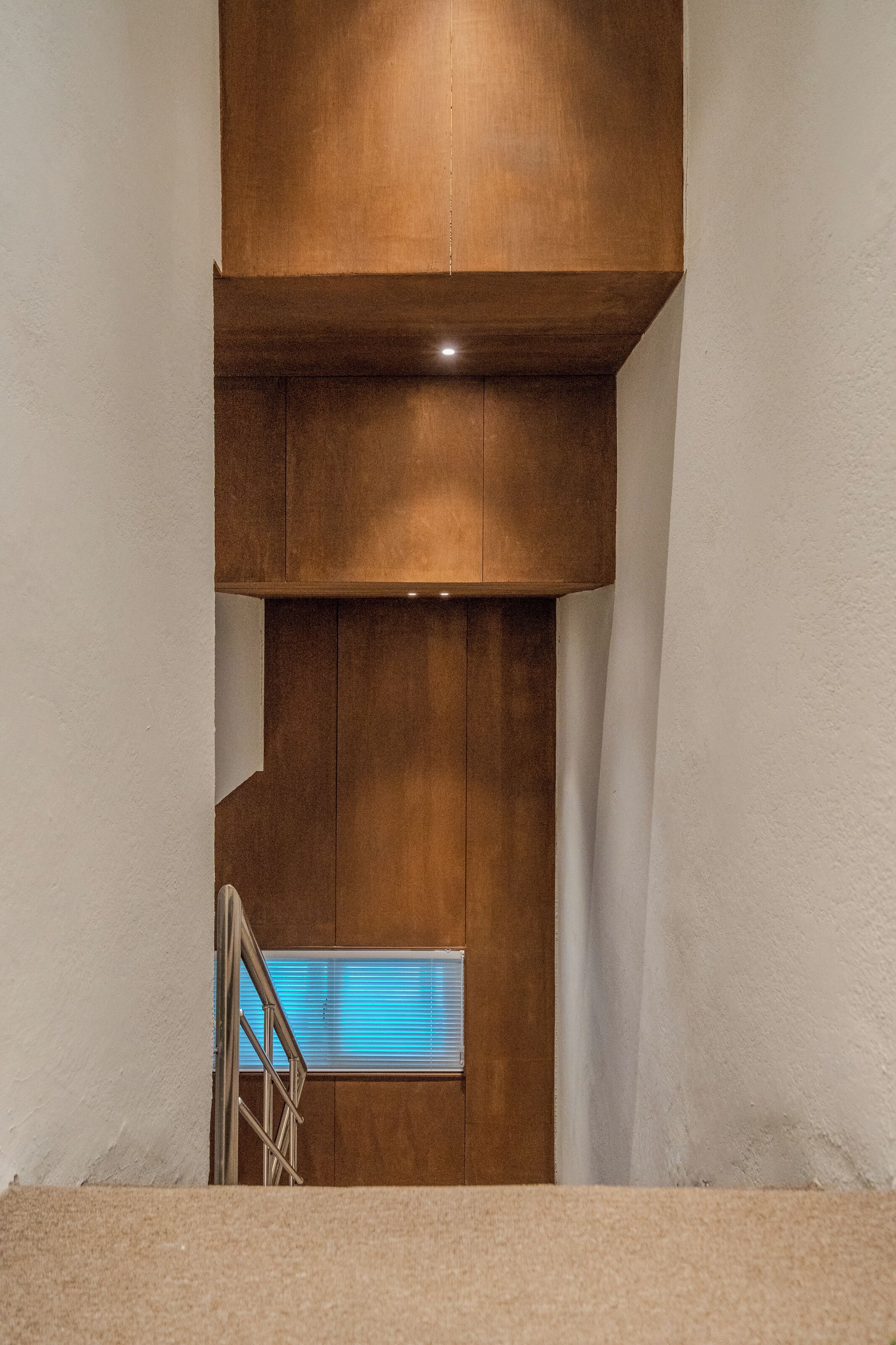 A narrow staircase with a wooden handrail and a window with blue blinds at the bottom.