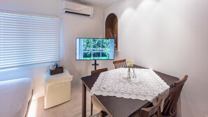 A dining area with a table covered by a lace tablecloth, a television mounted on the wall, and an air conditioning unit above the table. - Harujae Myeongdong (Seoul)