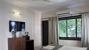 Una camera d'albergo con un letto, una televisione a parete, un mobiletto in legno, una finestra con tende e un condizionatore d'aria.