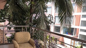 Un balcone con una divano, un tavolino in vetro con bevande e vista su una piscina e degli edifici.