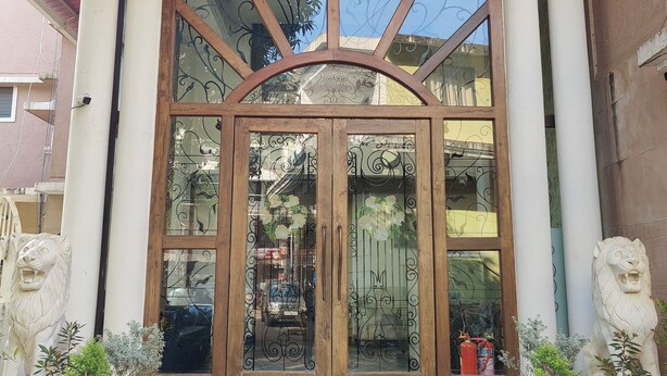 Un ingresso di un edificio con una porta in legno, ampie vetrate e due statue di leoni.