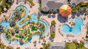 Luchtbeeld van een resort met meerdere zwembaden, ligbedden en een grote parasol.