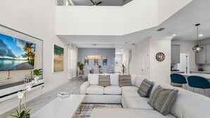 Een ruime woonkamer met een grote bank, een flatscreen-tv en een eethoek op de achtergrond.