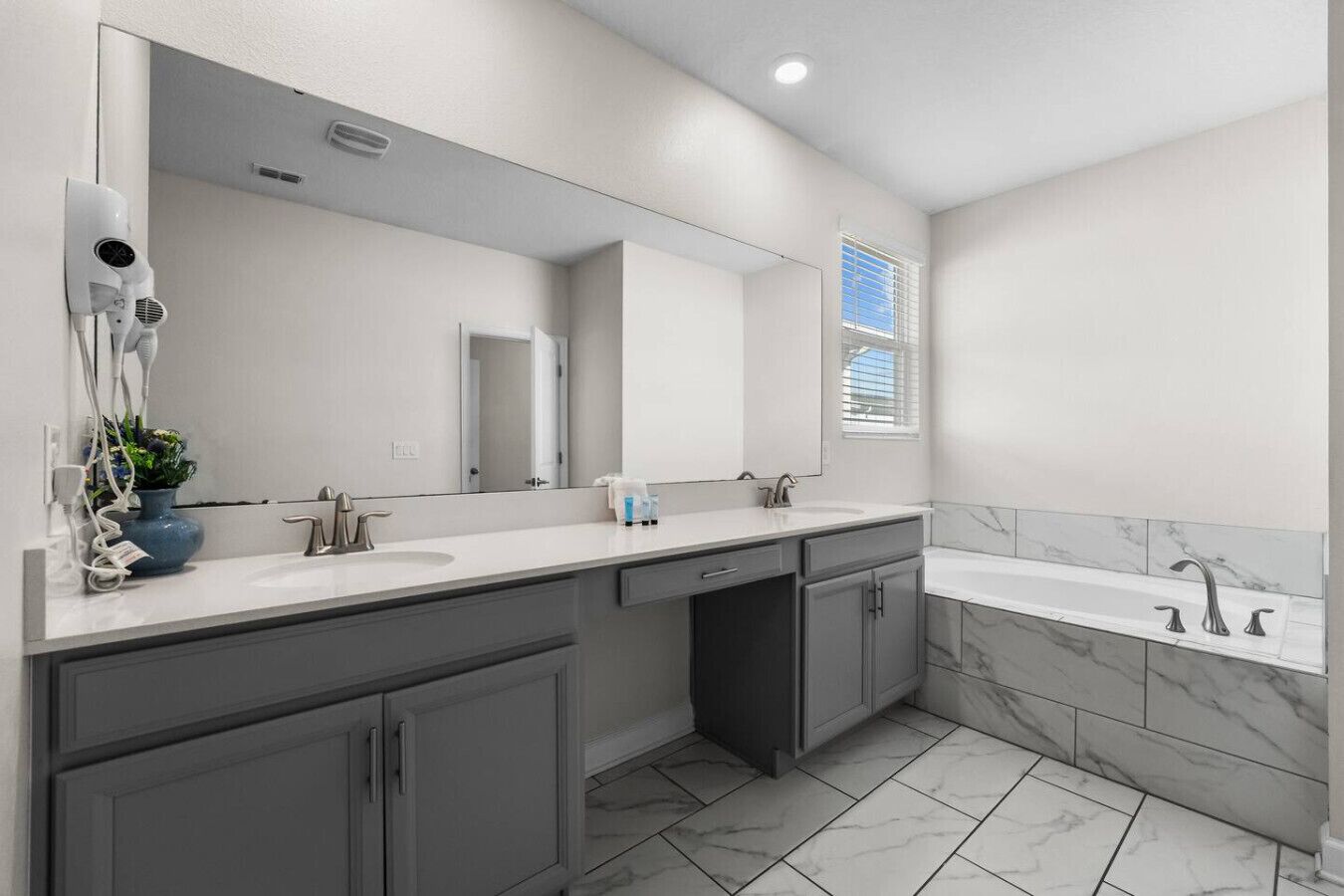 A modern bathroom with a large mirror, two sinks, a shower, and a hairdryer on the counter.