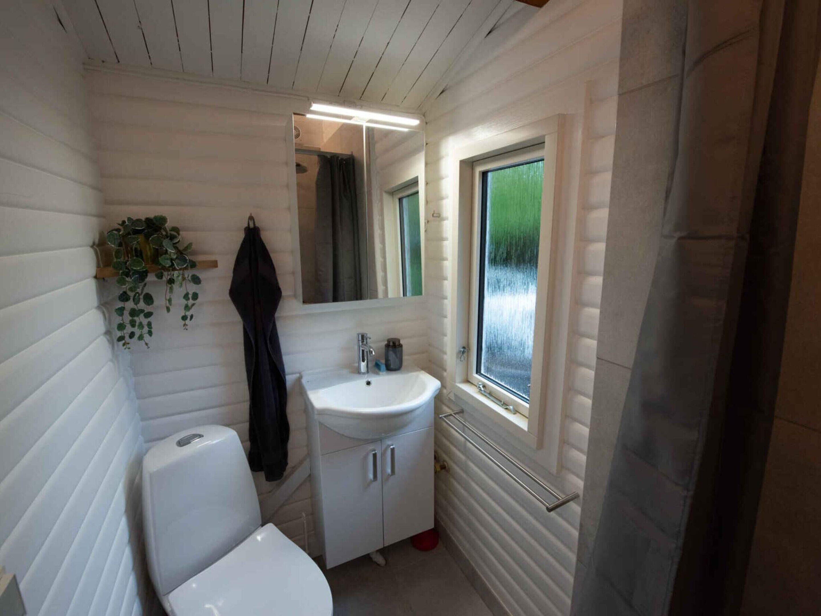 A compact bathroom with a white sink, toilet, and mirror. There is a window with a view of greenery outside.