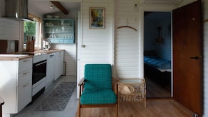 Une cuisine compacte avec des meubles blancs, un plan de travail en bois et un coin repas comprenant une chaise turquoise et une petite table en osier.