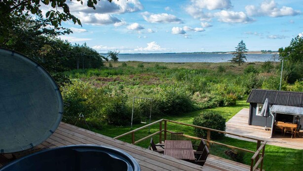 Une terrasse en bois avec un jacuzzi, une balançoire et un petit bâtiment doté d’un espace salon extérieur.