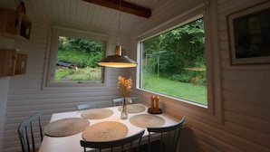 Un coin repas avec une table dressée pour quatre personnes, entourée de chaises en bois, d’une suspension et d’un vase rempli de fleurs.