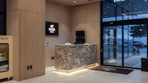 Una moderna zona de recepción con mostrador de mármol, paneles de madera y un gran ventanal que da al exterior.