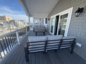 A covered outdoor deck with a sofa and a table, a railing, and a view of the cityscape. - BEACHBLOCK HOUSE WITH PRIVATE POOL OCEANVIEW 2 DECKS 4 MASTER NEAR BOARDWALK (North Wildwood)